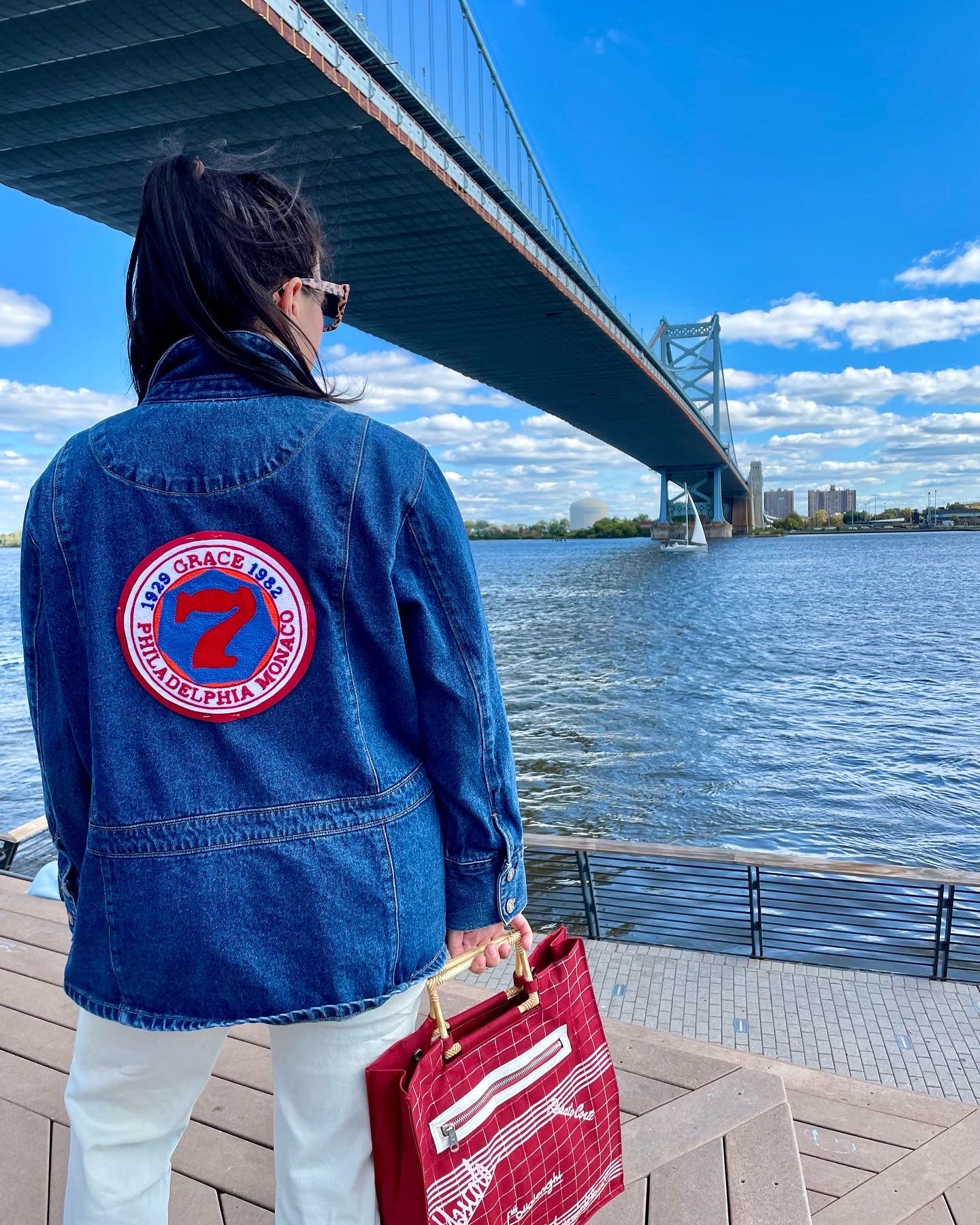 photo of a woman standing on a pier in a denim jacket with a custom chainstitched circular patch.  The patch has the number 7 on it with text around it in a circle 