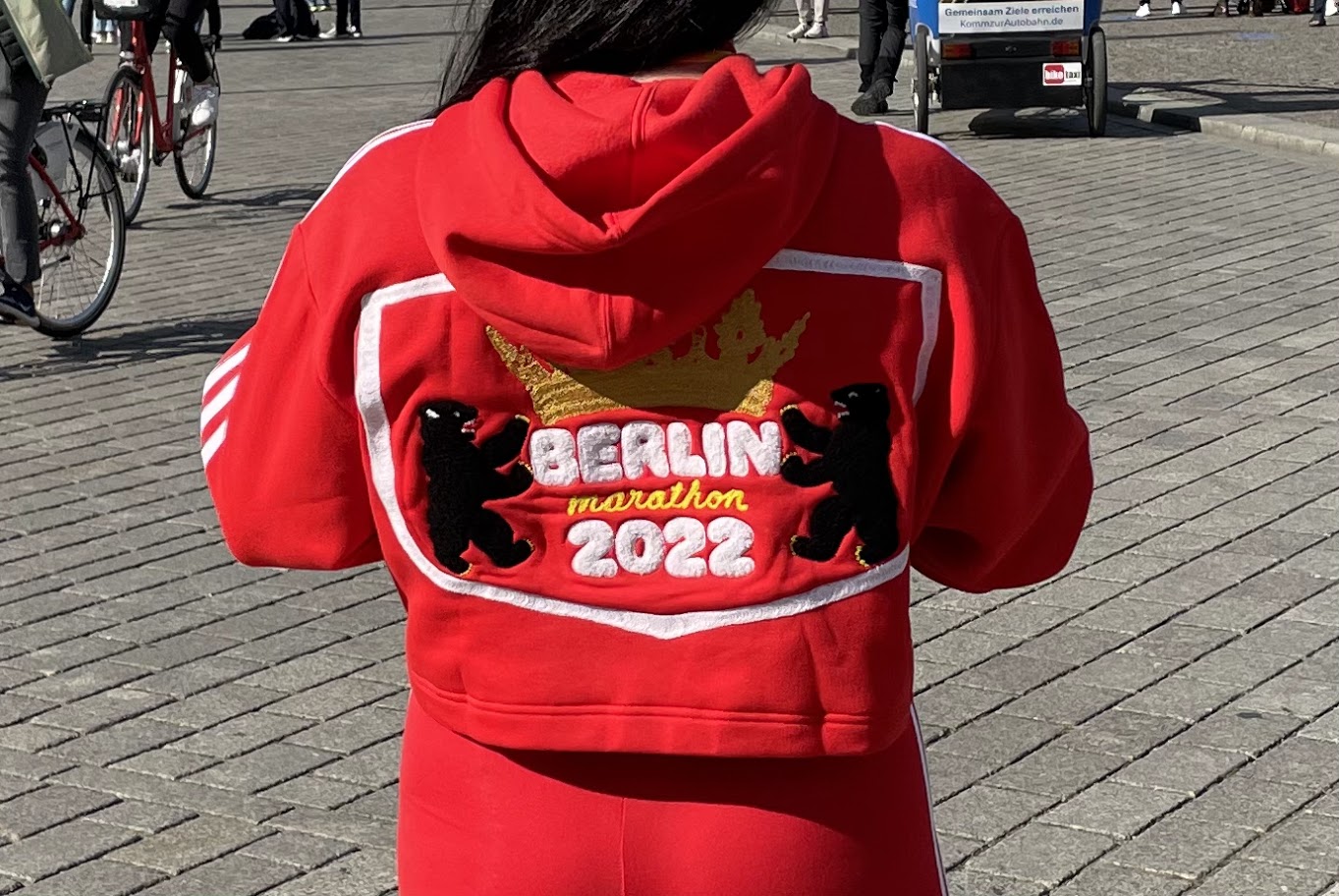 photo of a woman wearing an adidas red hooded sweatshirt with a custom chainstitched logo  that says Berlin Marathon 2022.  It features a crown and two Berliner bears inside the crest of the city.