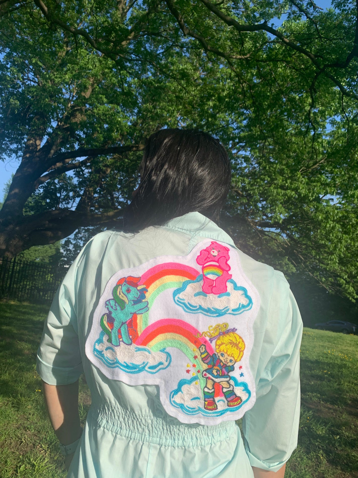 photo of a woman wearing a jumpsuit chainstitched with 80s cartoons featuring a care bear, a my little pony, and a rainbow brite.